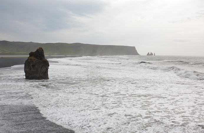 View from Dyrholaey northeast to Vik, showing Reynisdrangar, the spiky basalt sea stacks formed when two trolls were unable to land their three-masted ship before dawn and thus turned to stone by the sunlight.